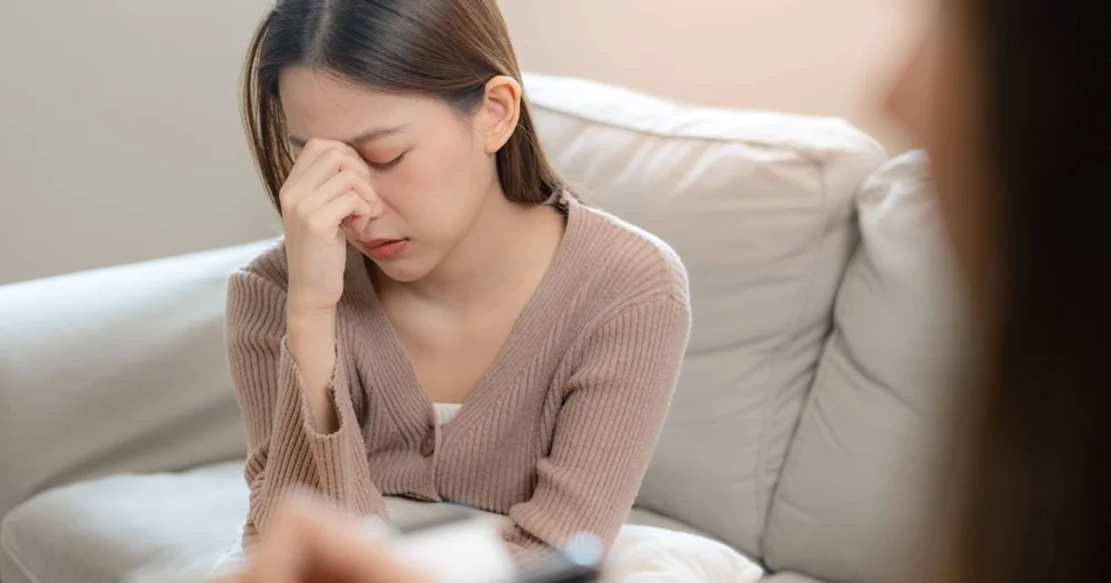A distressed woman sitting on a couch, holding her hand to her face, during a Stress Management session in Los Angeles and Beverly Hills.
