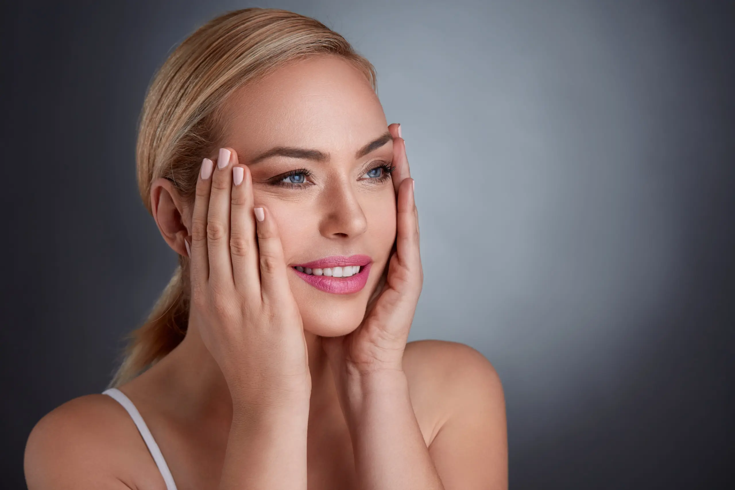 Close-up portrait of a smiling woman with clear, radiant skin touching her face, representing exosome skin therapy in Beverly Hills